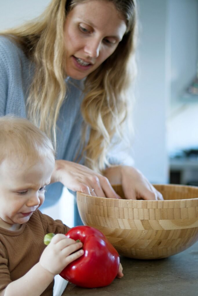 Mother and toddler cooking together, toddler holding a red bell pepper.